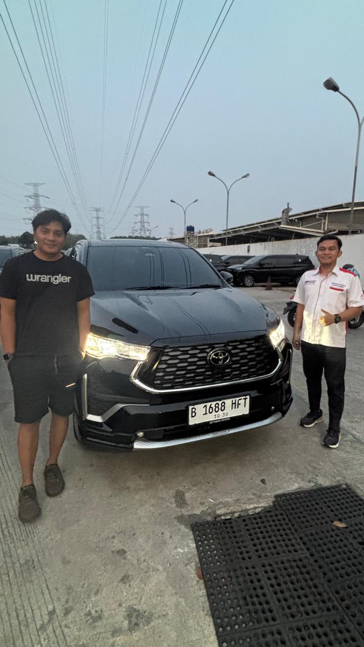 Dua orang berdiri di sisi depan sebuah kendaraan hitam.