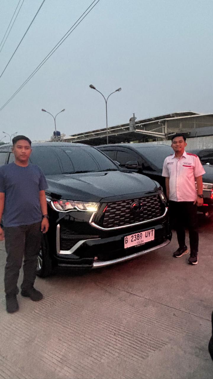 Dua orang berdiri di depan sebuah kendaraan hitam.